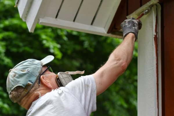 A man painting house exterior with white color